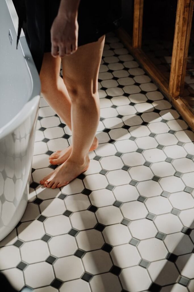 A young woman stands barefoot on sunlit tiled bathroom floor, emphasizing relaxation.