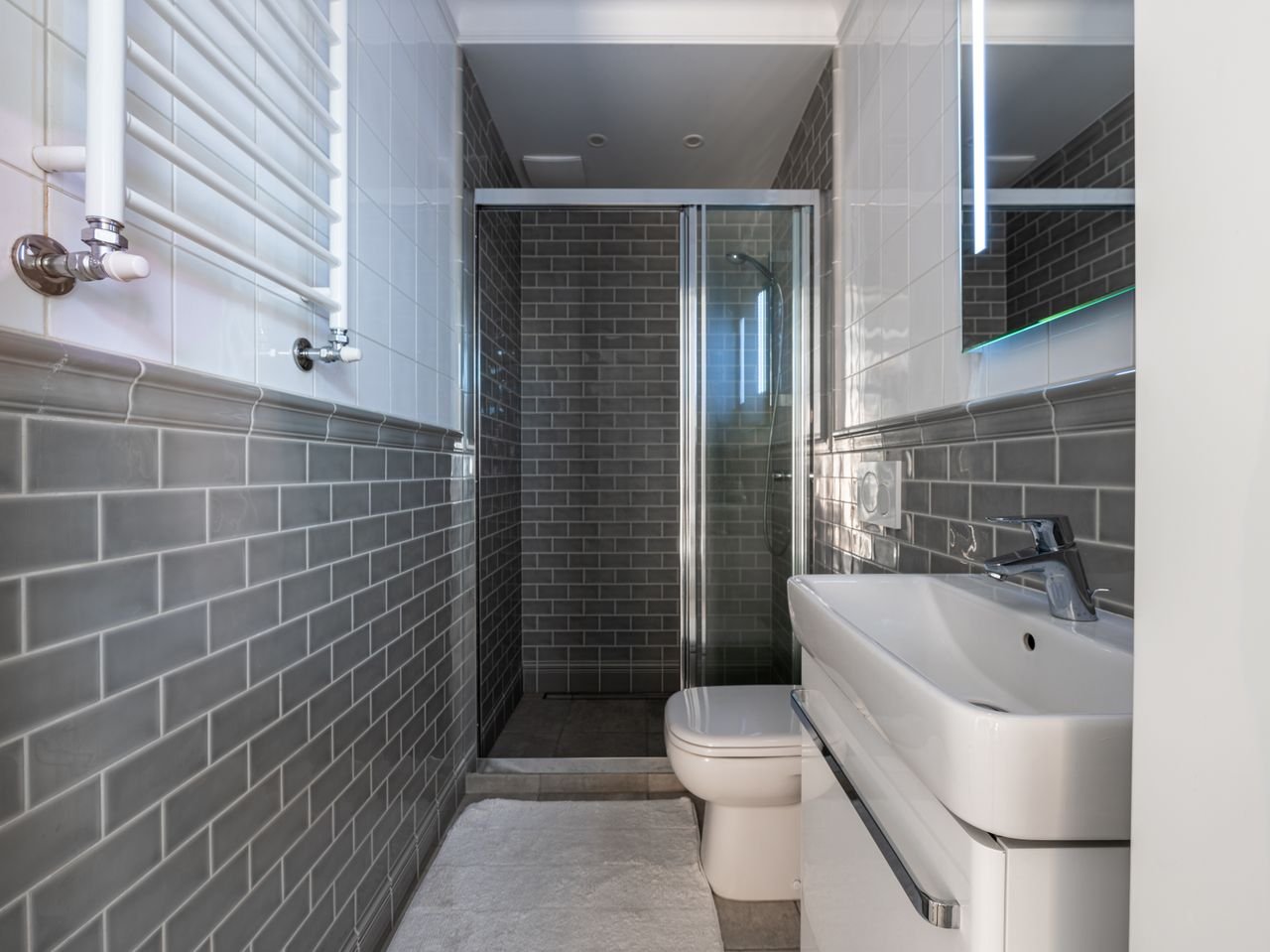 Compact bathroom featuring sleek fixtures and gray subway tiles with a glass-enclosed shower area.