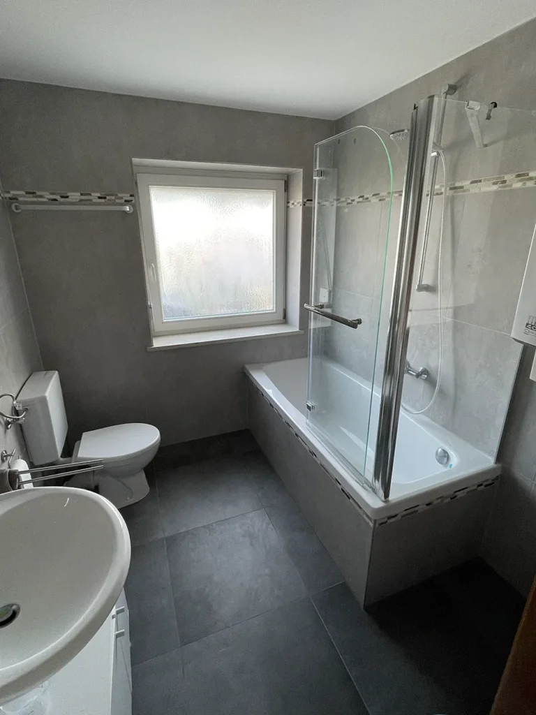 Modernisiertes Badezimmer mit stilvollen grauen Wand- und Bodenfliesen sowie Glaskabine.